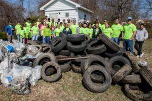 Numerous people in lime green shirts stand behind a large pile of rubber tires and other debris removed from a stream.