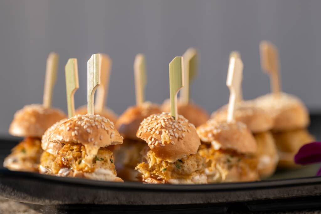A plate of mini crab cake sandwiches with sesame seed buns.
