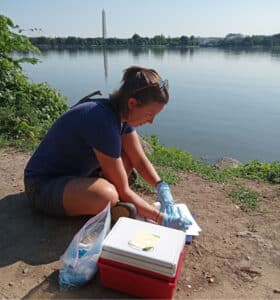 A person sitting by the water and writing, with the Washington Monument in the background