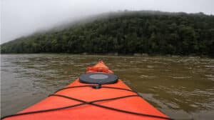 The front of a kayak looking toward a hill covered in fog.