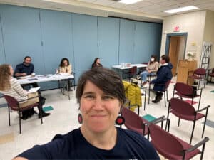 A person taking a selfie with others talking in a classroom in the background