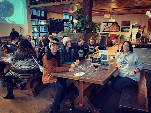 A crowd of people smile as they sit around a table drinking beer.