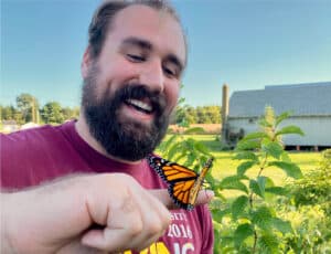 A person smiling while a monarch butterfly rests on their finger