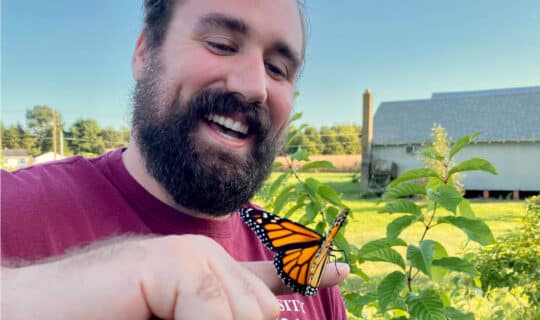 A person smiling while a monarch butterfly rests on their finger