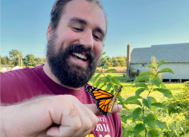 A person smiling while a monarch butterfly rests on their finger