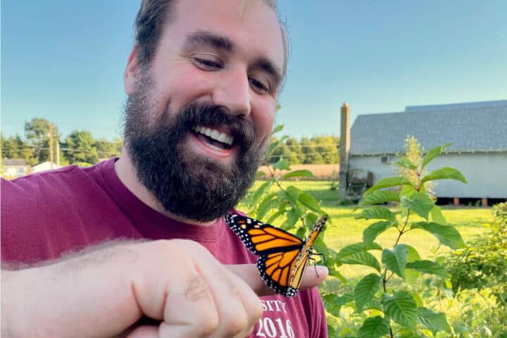 A person smiling while a monarch butterfly rests on their finger