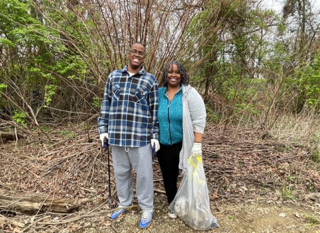 Two people smiling and holding trash bags.