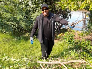 A person holding smiling while holding vines near a river.