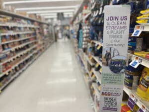 A sign reading "Join us to Clean Streams and Plant Trees" in a grocery store aisle.