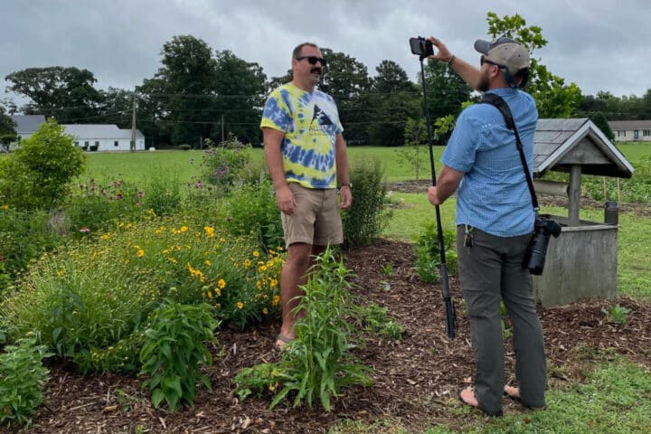 A person filming someone speaking in a garden