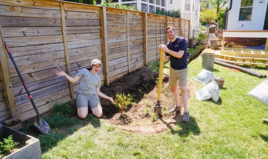 To people smiling as they stand next to a rain garden being established