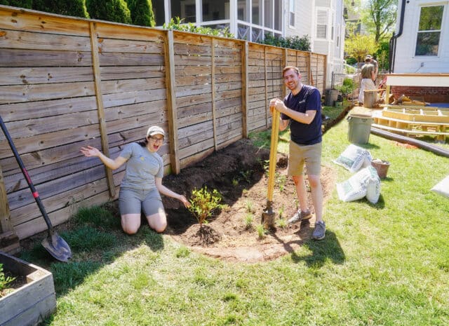 To people smiling as they stand next to a rain garden being established