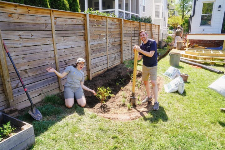 To people smiling as they stand next to a rain garden being established