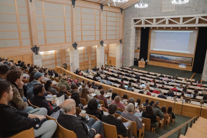 An auditorium full of people, listening to a speaker in the distance