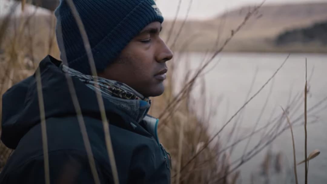 A side profile of a person standing next to a river with their eyes closed