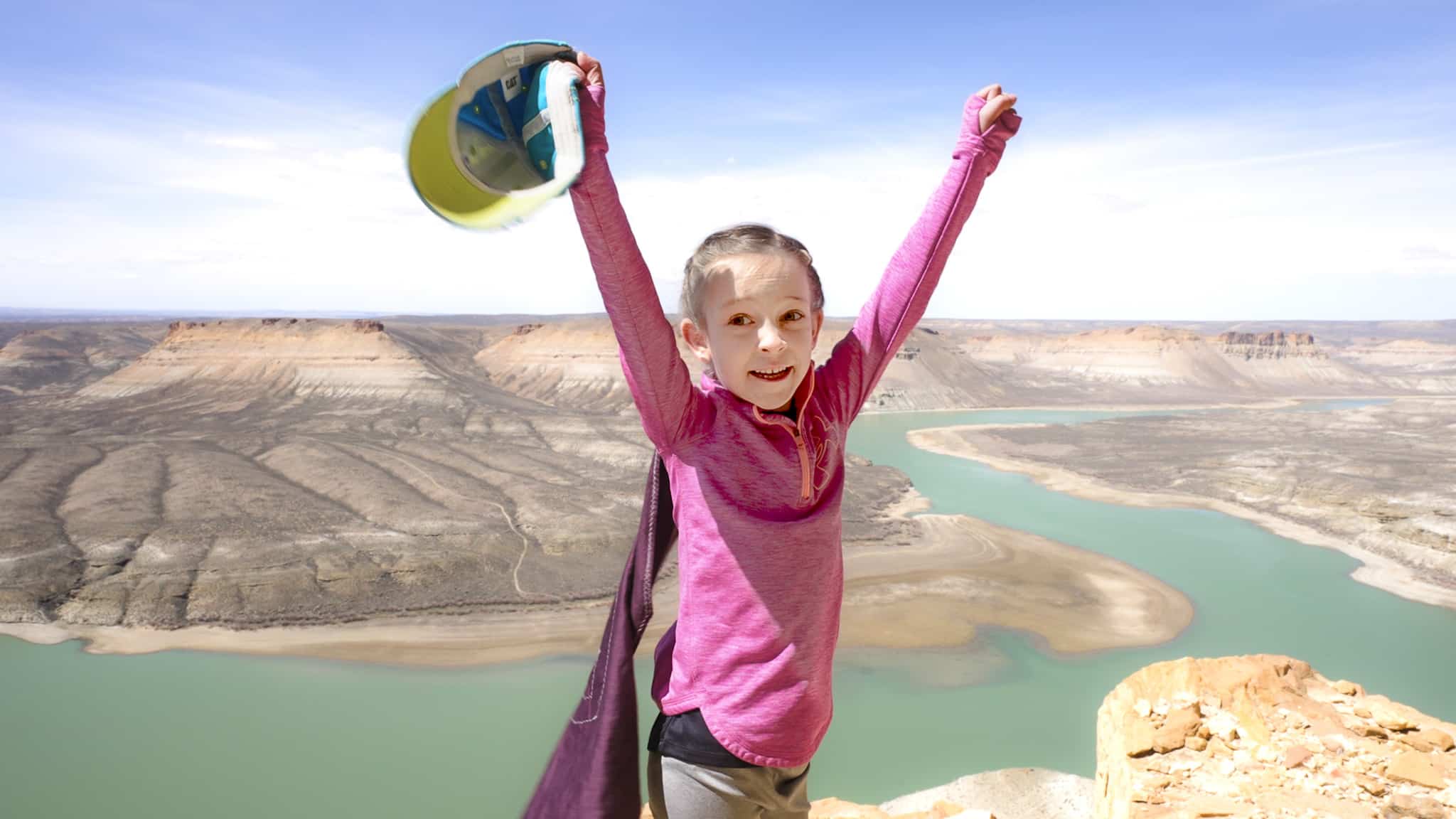 A young person celebrating with their arms help up on top of a mountain