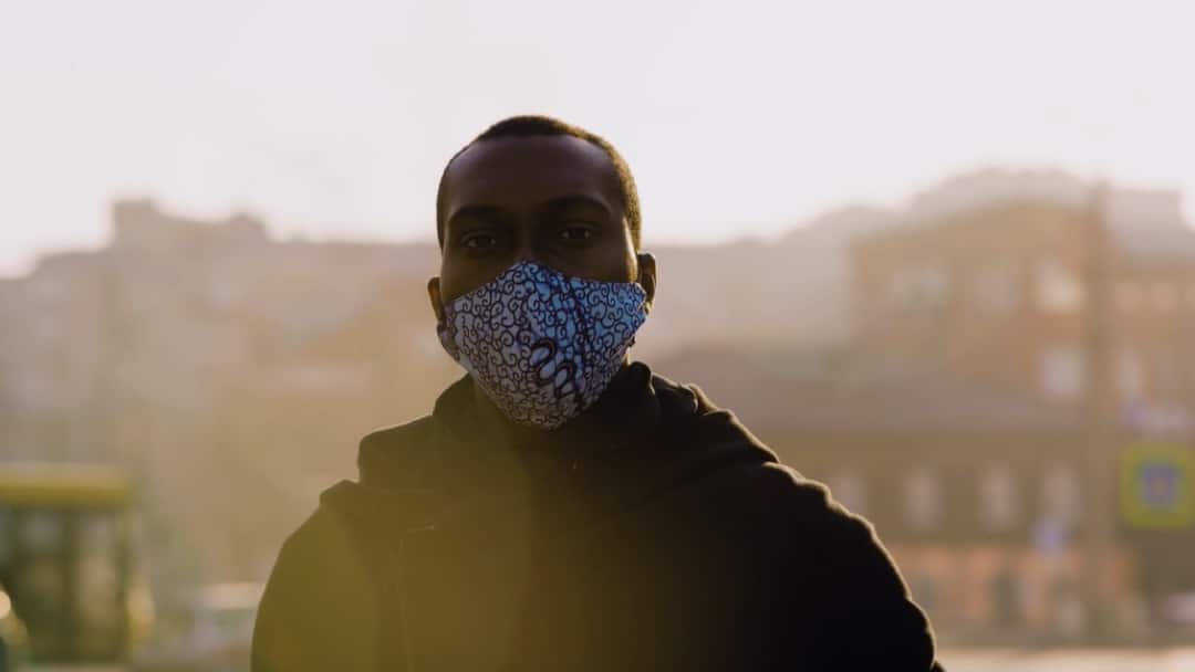 A person in a mask standing in the foreground, with a city in the background