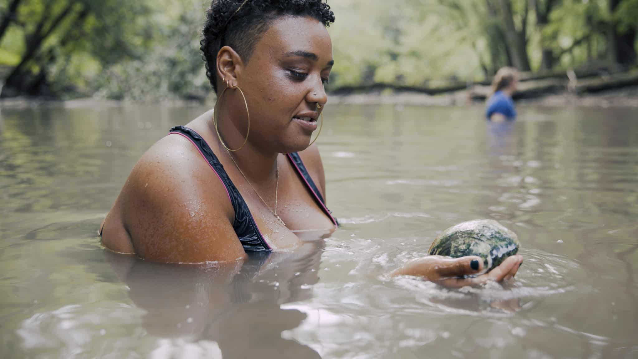 A person in a bathing suit holding a mussel in a river