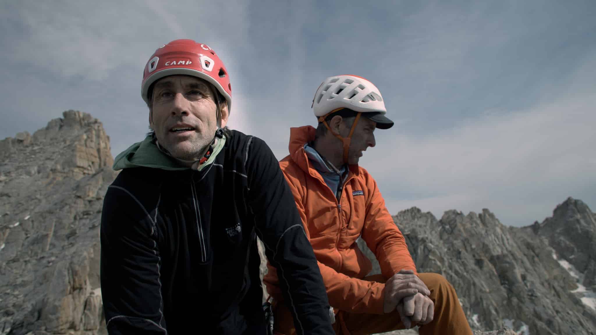 Two people in climbing helmets sitting on top of a mountain/rock face