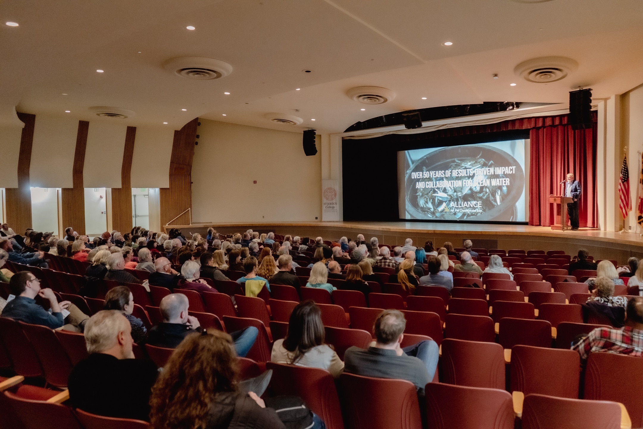 People in a theater, listening to opening remarks.