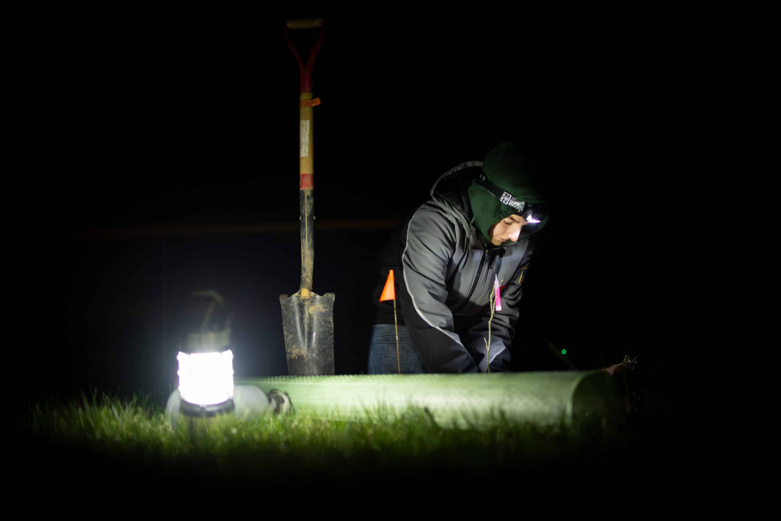 A person with a headlamp plants a tree seedling in a field