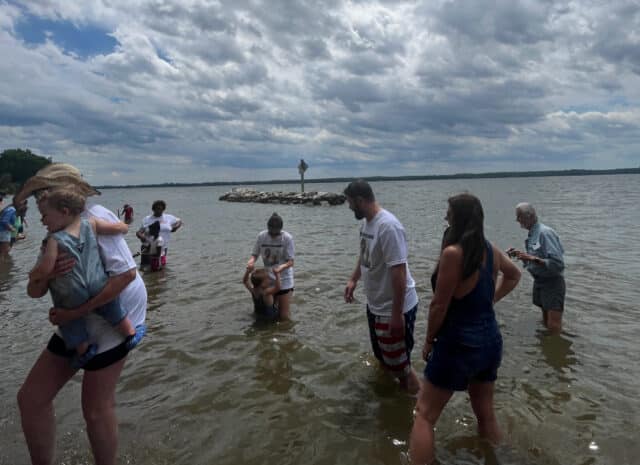 A group of people wade into the the side of a river