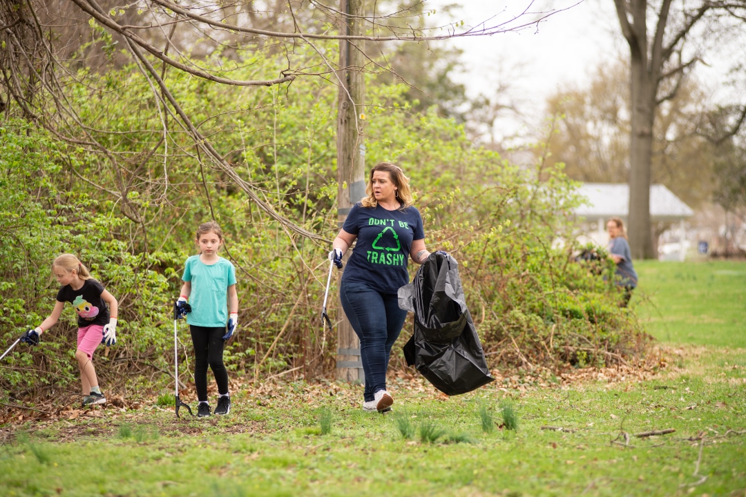 Children and adults clean up trash with grabbers