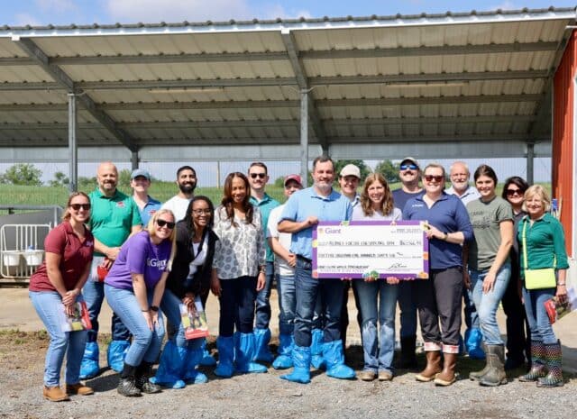 A group of people stand around a large check on a farm property.