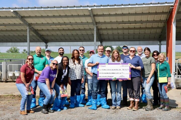 A group of people stand around a large check on a farm property.