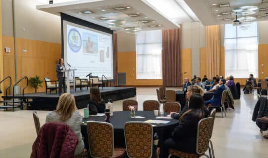 a room of people watch a speaker on stage