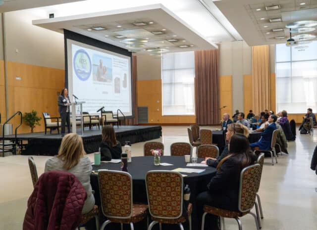 a room of people watch a speaker on stage