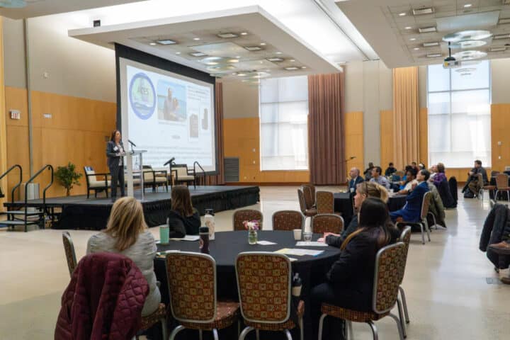 a room of people watch a speaker on stage