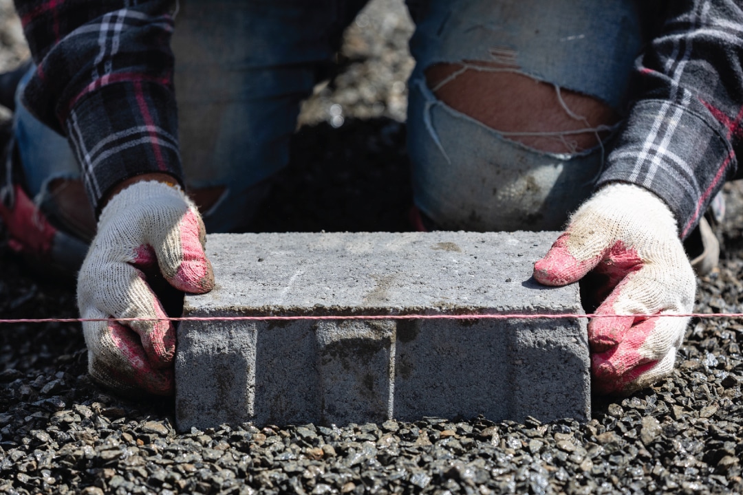 a close up of someone laying a gray brick onto gravel