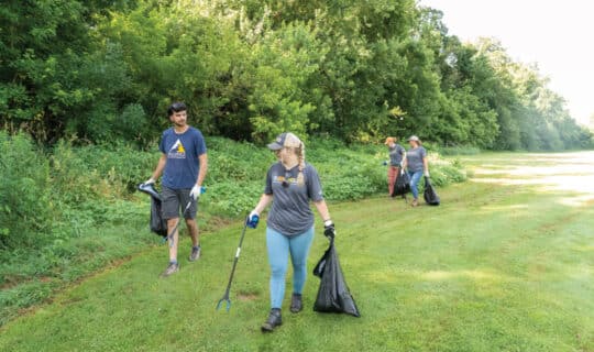 a group of people walk along a tree line with trash bags and trash grabbers