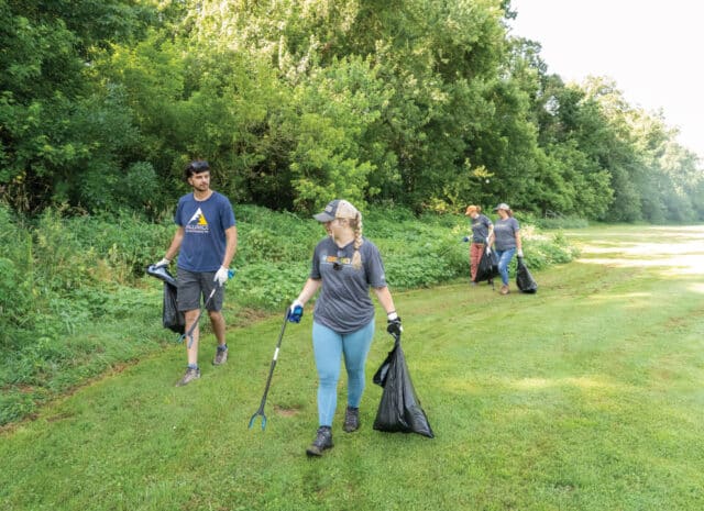 a group of people walk along a tree line with trash bags and trash grabbers