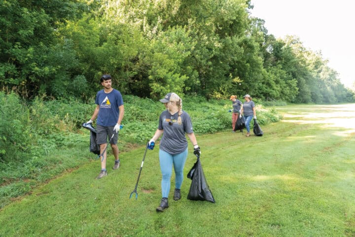 a group of people walk along a tree line with trash bags and trash grabbers