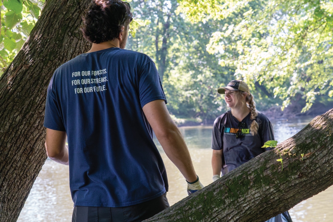 two people stand by a tree next to a river