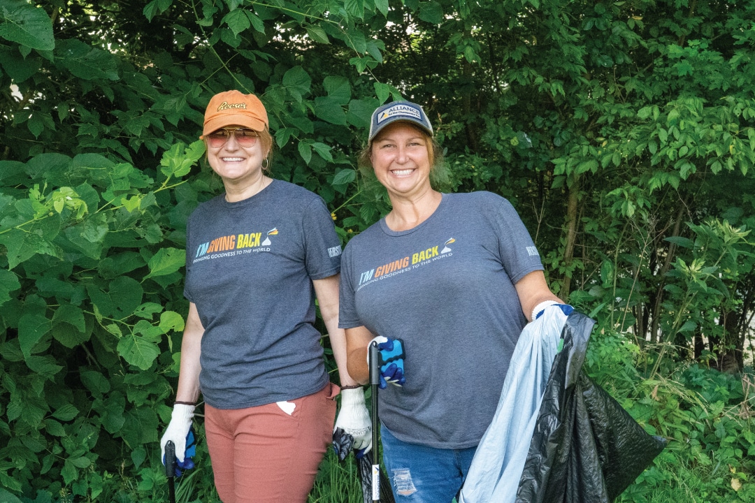 two people smiling while holding trash bags and trash grabbers