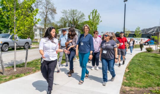A person speaks to a group of people while leading them down a sidewalk