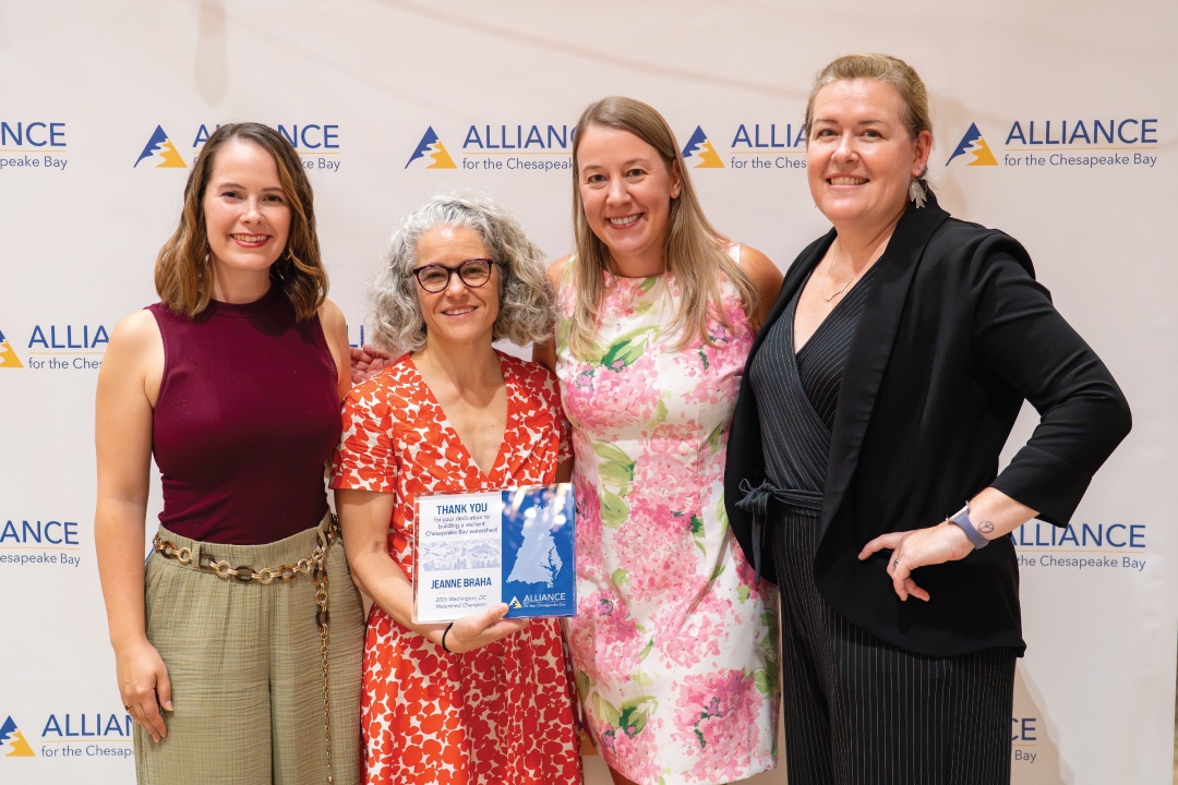 four people pose for a picture, the person second from the left holds an award plaque