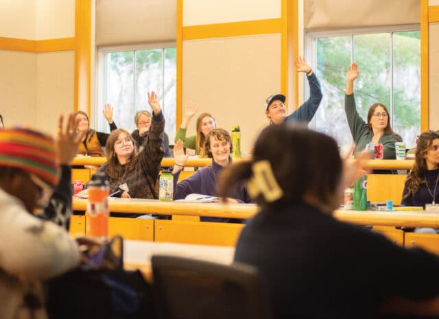 Rows of people in a lecture hall raise their hands
