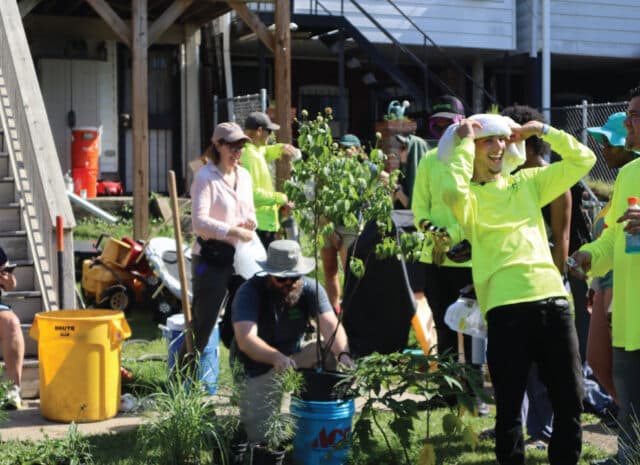 people in a yard smile and plant trees and grasses