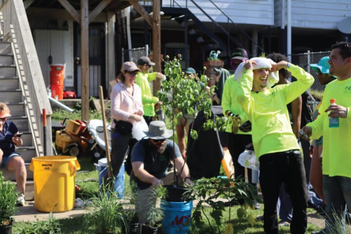 people in a yard smile and plant trees and grasses