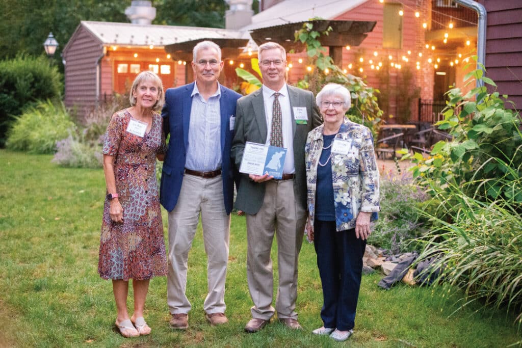 Four people pose for a photo with one of them holding an award plaque
