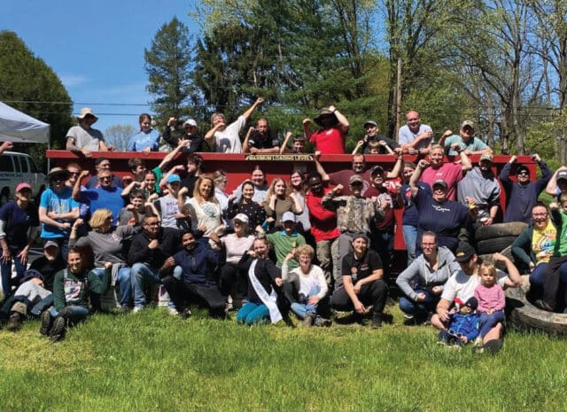 a large group of people flex their arms in celebration during a clean up event