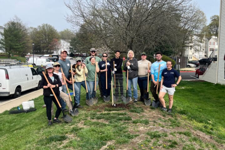 a group of people pose for a group photo around a newly-planted tree