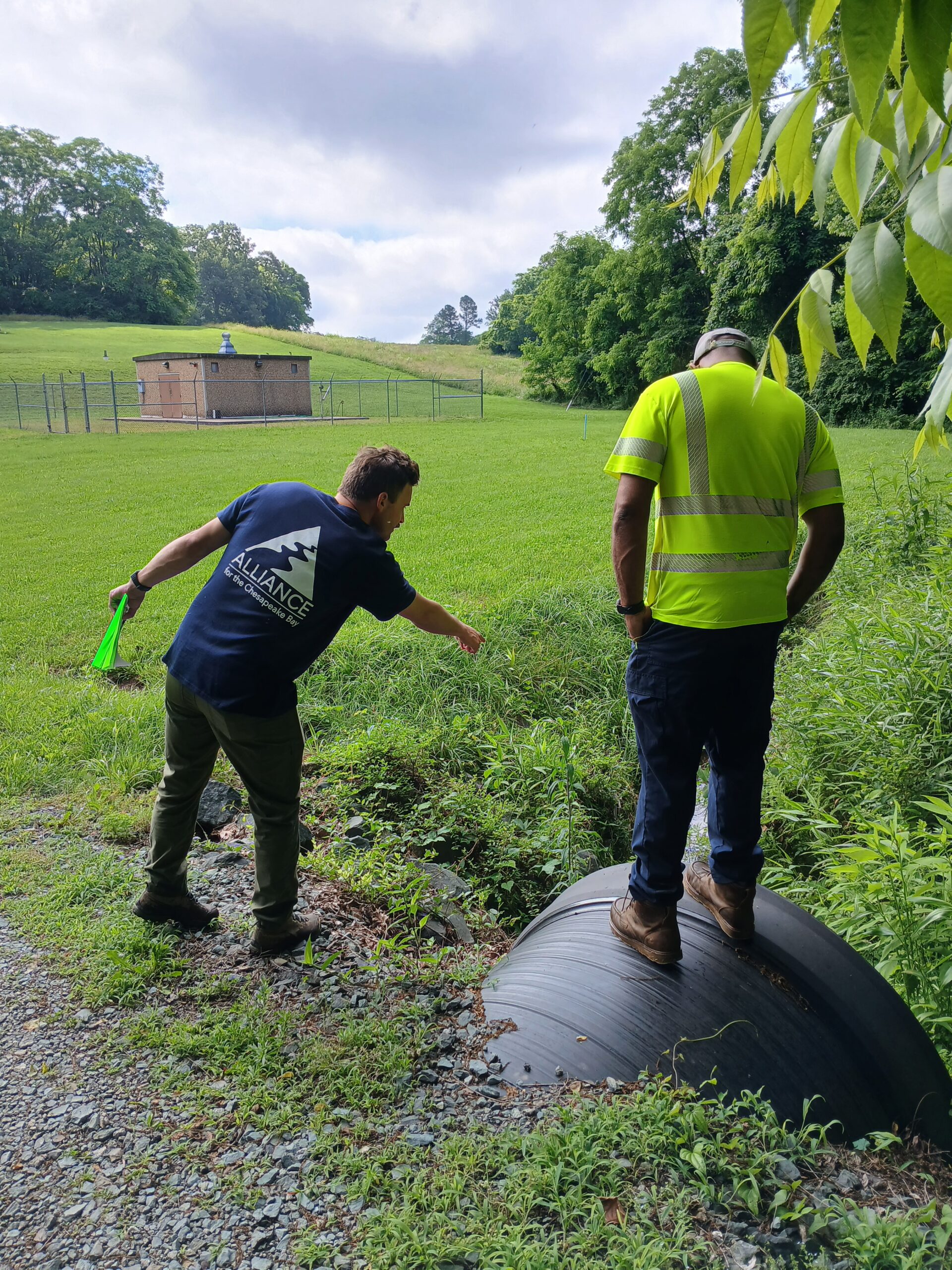 A person standing and pointing down at a culvert while a second person looks down.