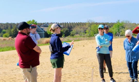 people stand on a beach and smile while listening to someone speak