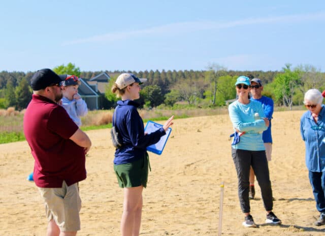 people stand on a beach and smile while listening to someone speak