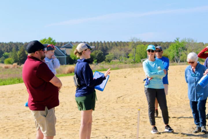 people stand on a beach and smile while listening to someone speak